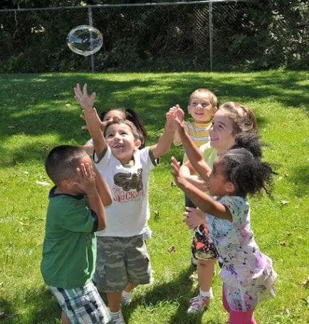 Children reaching for a bubble in a grassy yard.