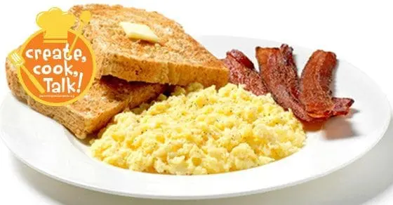 Scrambled eggs, toast with butter, and bacon on a white plate with a "create. cook. Talk!" logo.