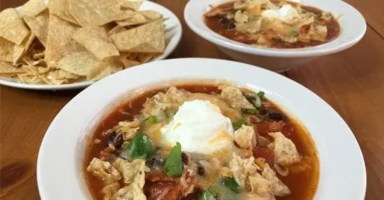 Bowls of chicken tortilla soup topped with cheese and a side of tortilla chips.