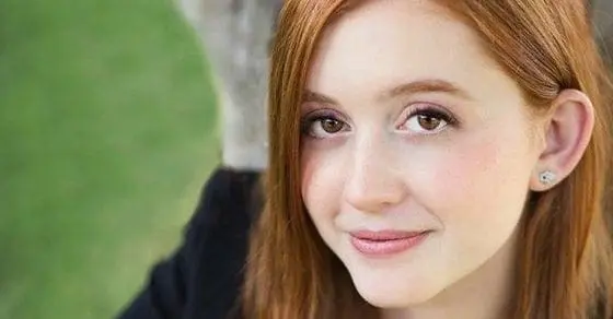 Young woman with red hair smiles outdoors.
