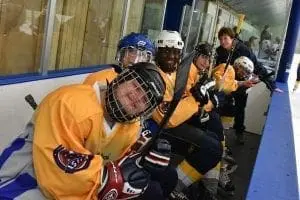 Hockey players in yellow jerseys sit in a dugout.