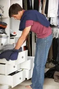 A young man sorts clothes in a cluttered closet.