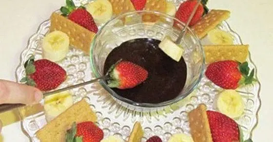 Chocolate fondue with strawberries, bananas, and crackers on a platter.