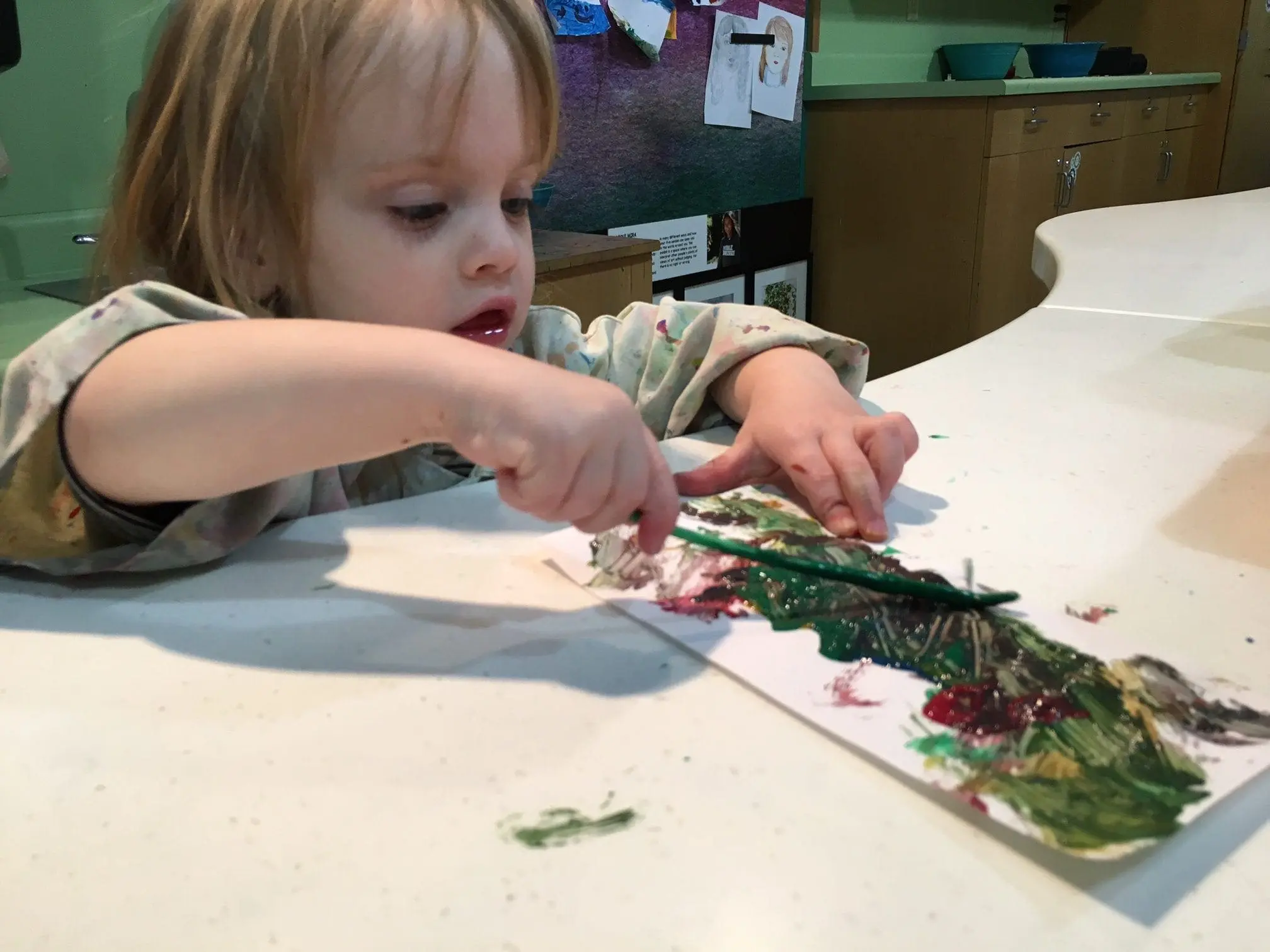 Child painting with green and red paint on a white surface.
