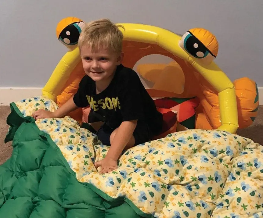 Boy sitting on a green comforter with a yellow blanket featuring a floral pattern.