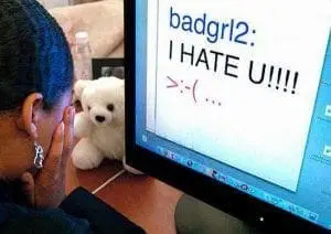 A person cries in front of a computer screen displaying a cyberbullying message.