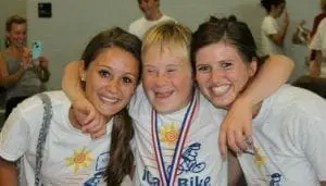 Three smiling people, two women with arms around a boy wearing a medal.
