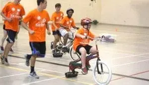 Children participating in the iCan Bike program ride specialized bicycles with trainers running alongside.