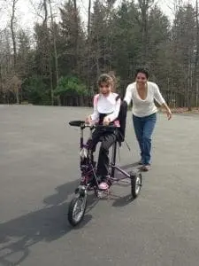 Nubia Smith walking behind a child in a mobility trike.
