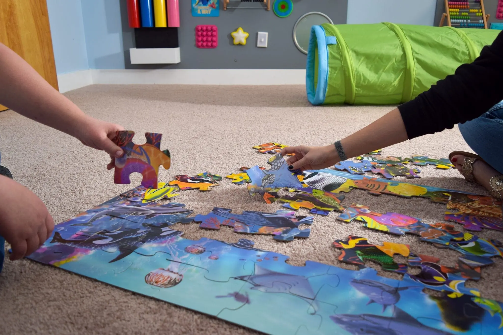 Two people assembling a puzzle on the floor in a room with sensory toys.