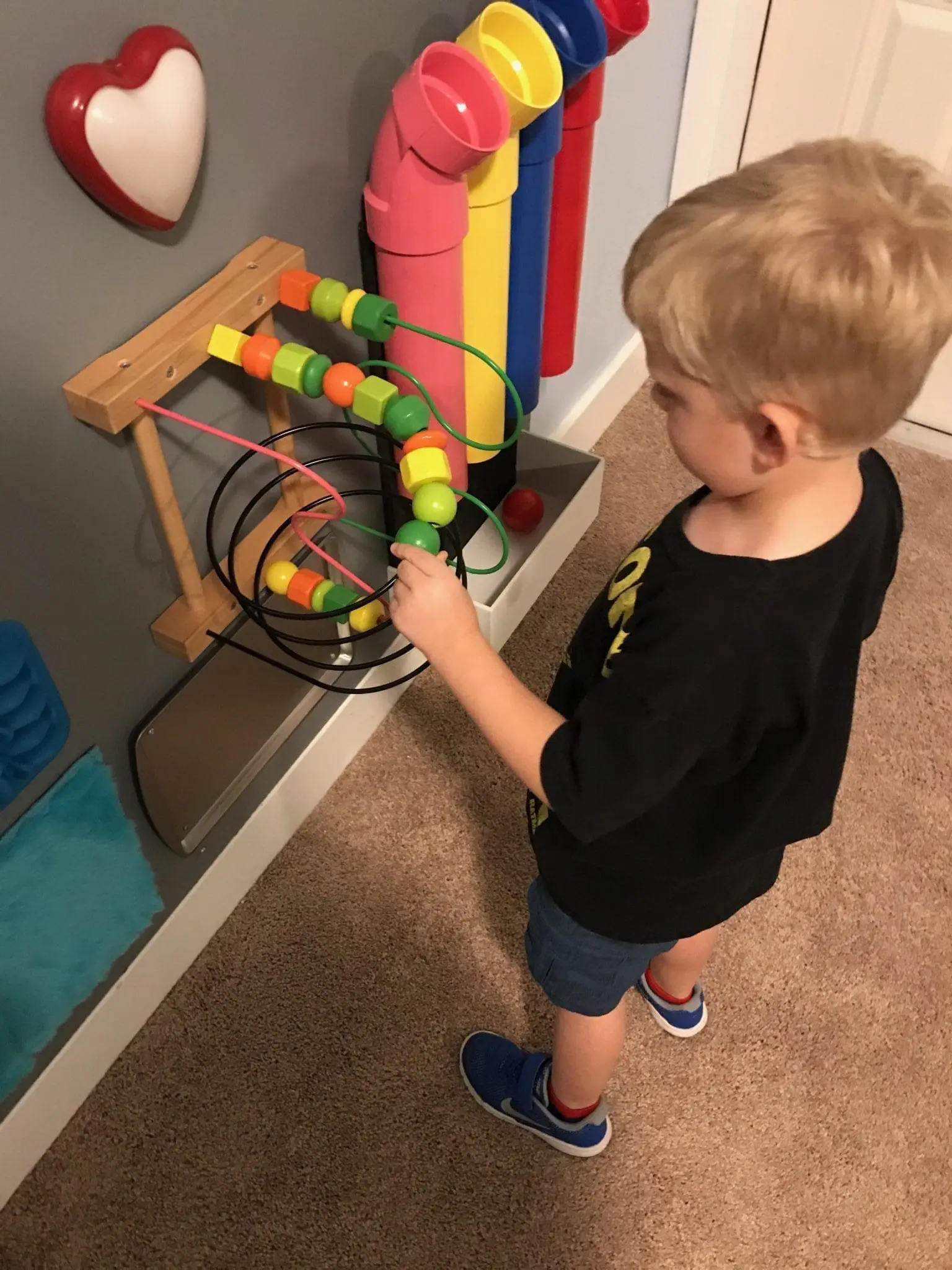 A young boy plays with a colorful bead maze attached to a sensory wall.
