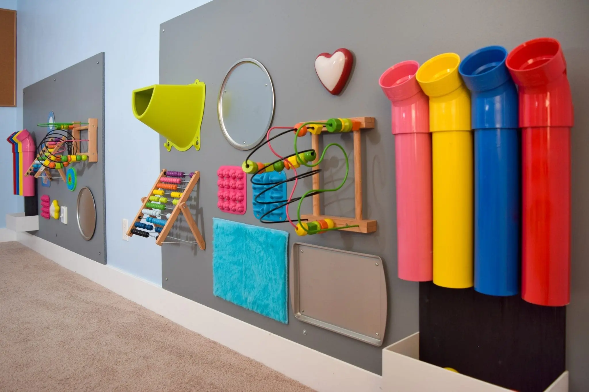 Sensory wall with various interactive elements including pipes, mirrors, and textured objects.