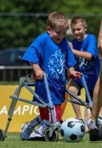 A boy with a walker smiles while playing soccer.