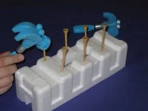 Golf tees stuck into a Styrofoam block with toy hammers nearby.