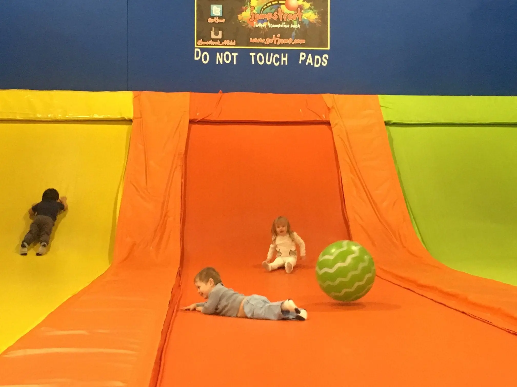 Children on a colorful inflatable slide at a trampoline park.