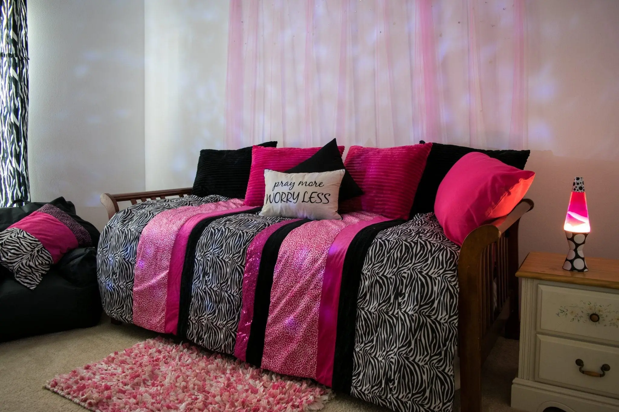 A daybed with pink and black zebra-striped bedding, pink throw pillows, and a "pray more worry less" pillow.