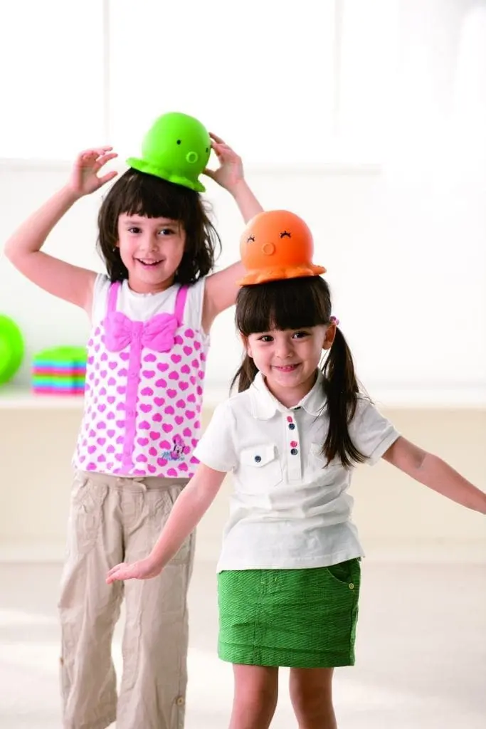 Two young girls balancing colorful octopus toys on their heads.