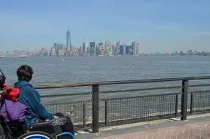 A person in a wheelchair looks out at the New York City skyline across the water.
