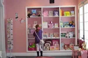 A young girl stands in front of a store display shelf filled with colorful items.