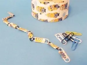 Paper clip bracelet with Minion characters next to a spool of Minion-themed tape and other paper clips.