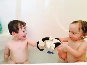 Two toddlers in a bathtub playing with a stuffed animal.