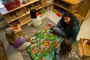 A woman smiles as she sits on the floor with three children playing with a mat and toys.