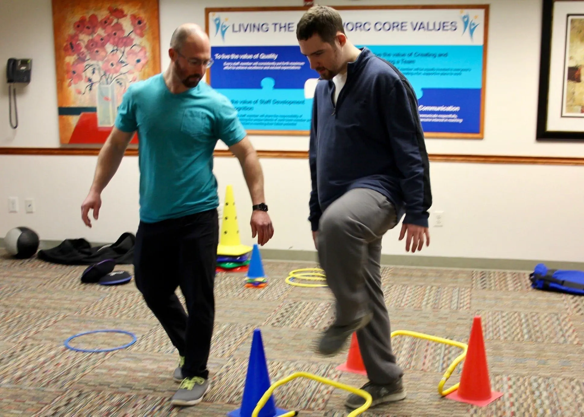 Two men participating in an adapted physical education exercise course with cones and hurdles.