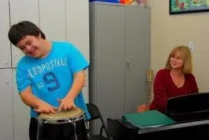 Riley plays a drum while Noreen Donnell watches him.