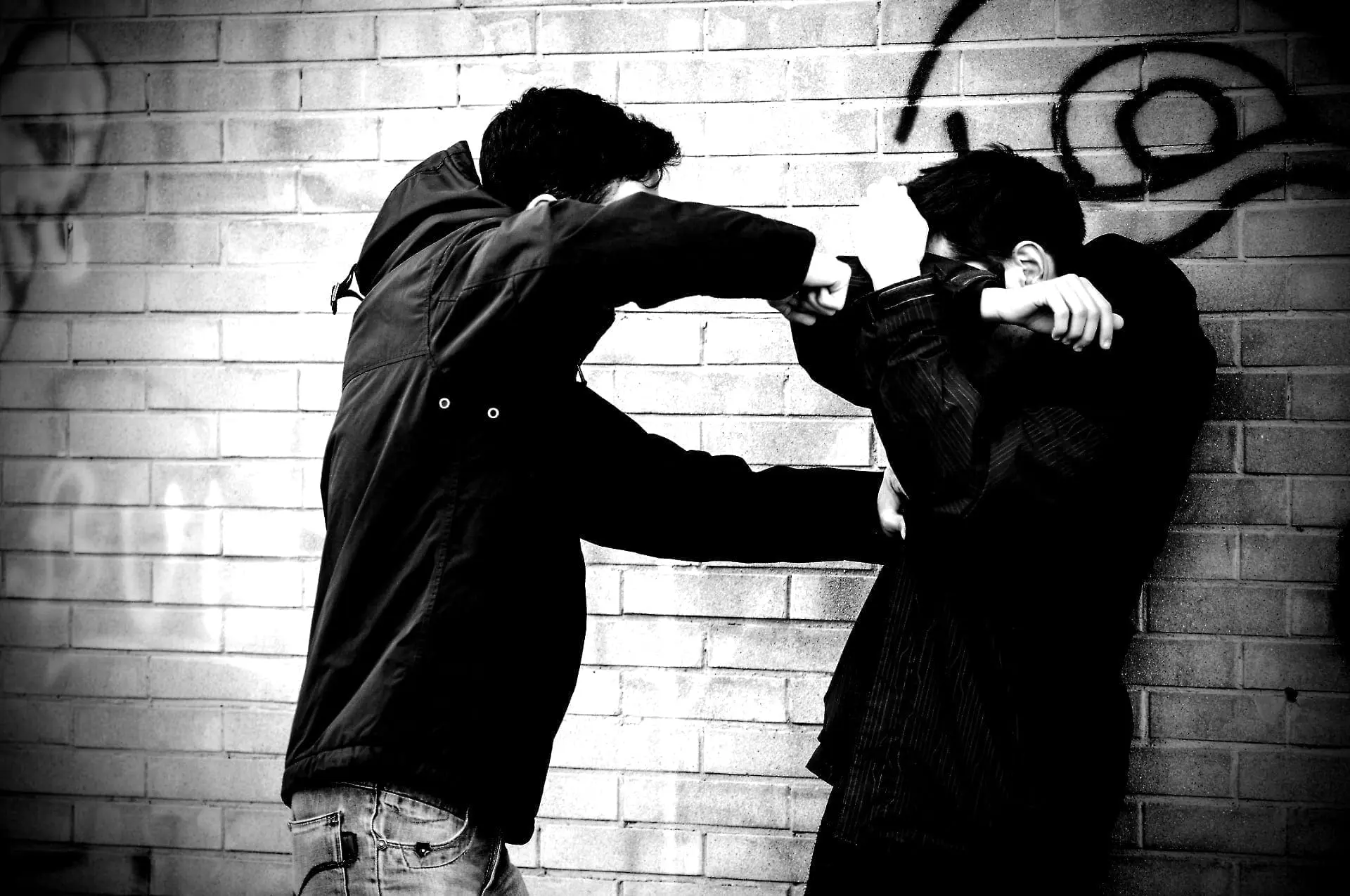 Two figures in a confrontation against a brick wall.