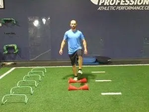 Man stepping over agility hurdles on a turf field.