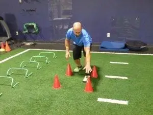 A man lunges forward, touching an orange cone with his left hand.