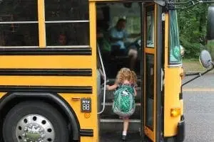Young girl with a backpack boarding a school bus.