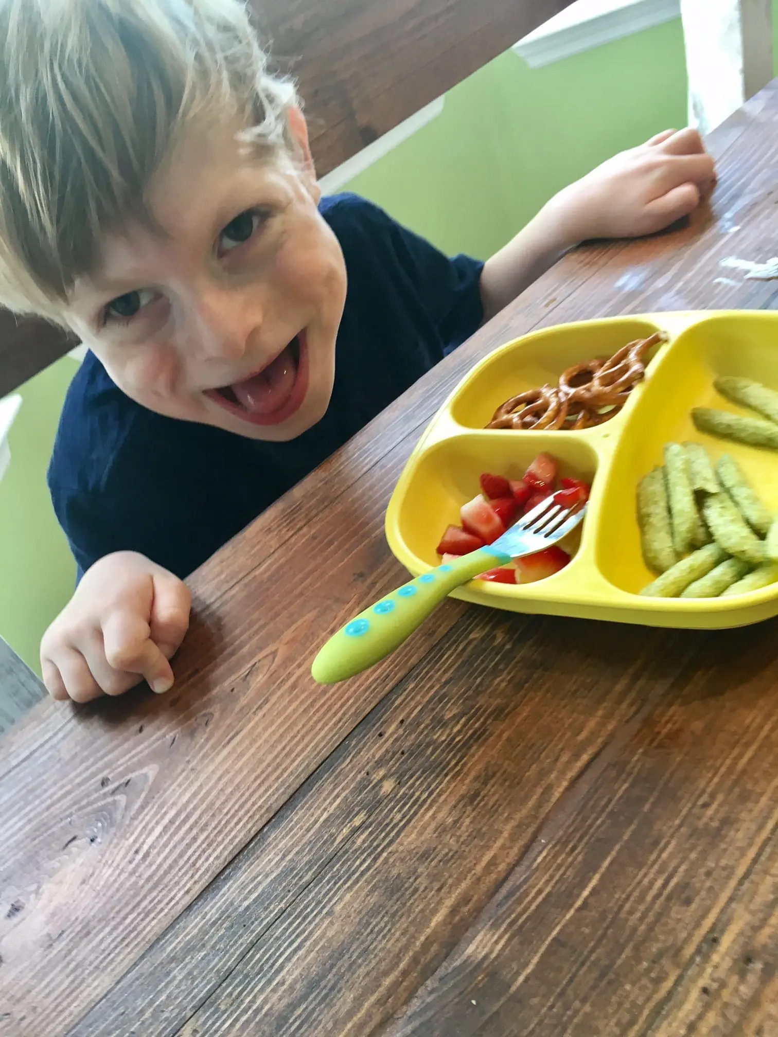 A young boy smiles with a divided plate of food in front of him.