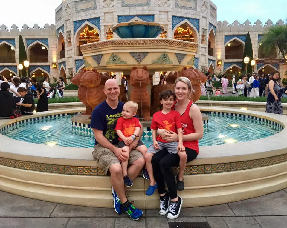 A family of four poses in front of a large fountain and ornate building.