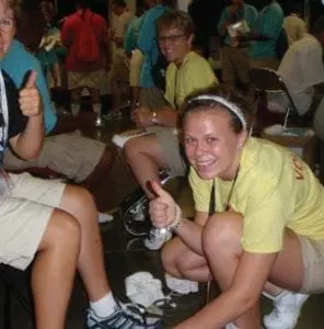 Two women wearing yellow shirts and khaki shorts give thumbs up.