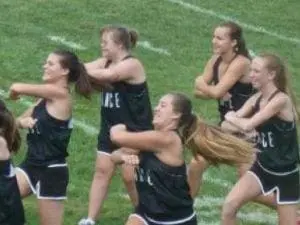 Cheerleaders in black uniforms perform a routine on a grassy field.