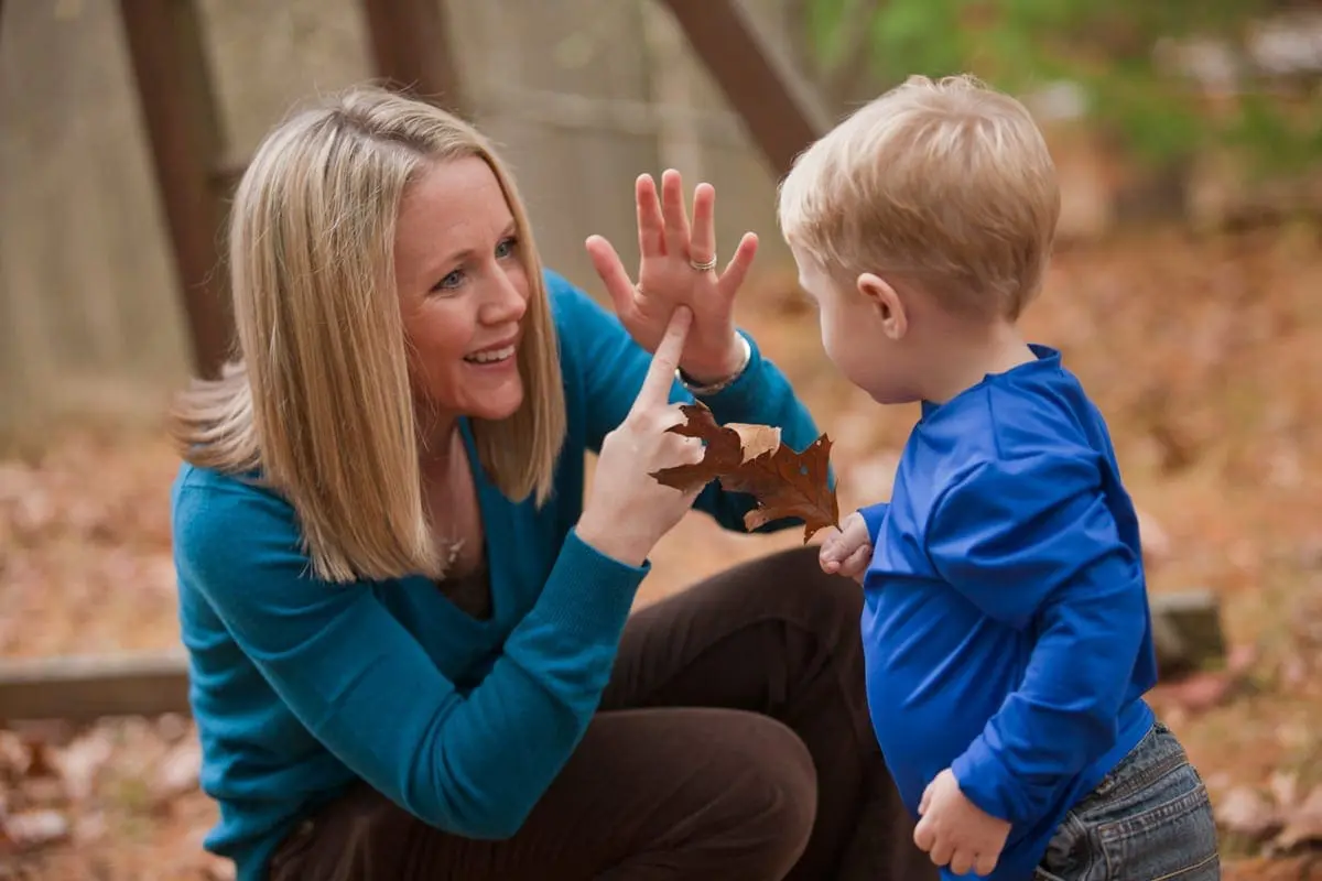 Therapist teaching a young child sign language outdoors.
