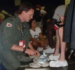 A man in a green uniform attaches elastic shoelaces to a shoe.