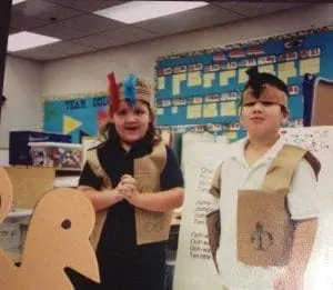 Two children in costumes stand in a classroom.