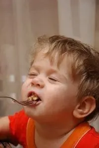 Young child with eyes closed eating from a fork.