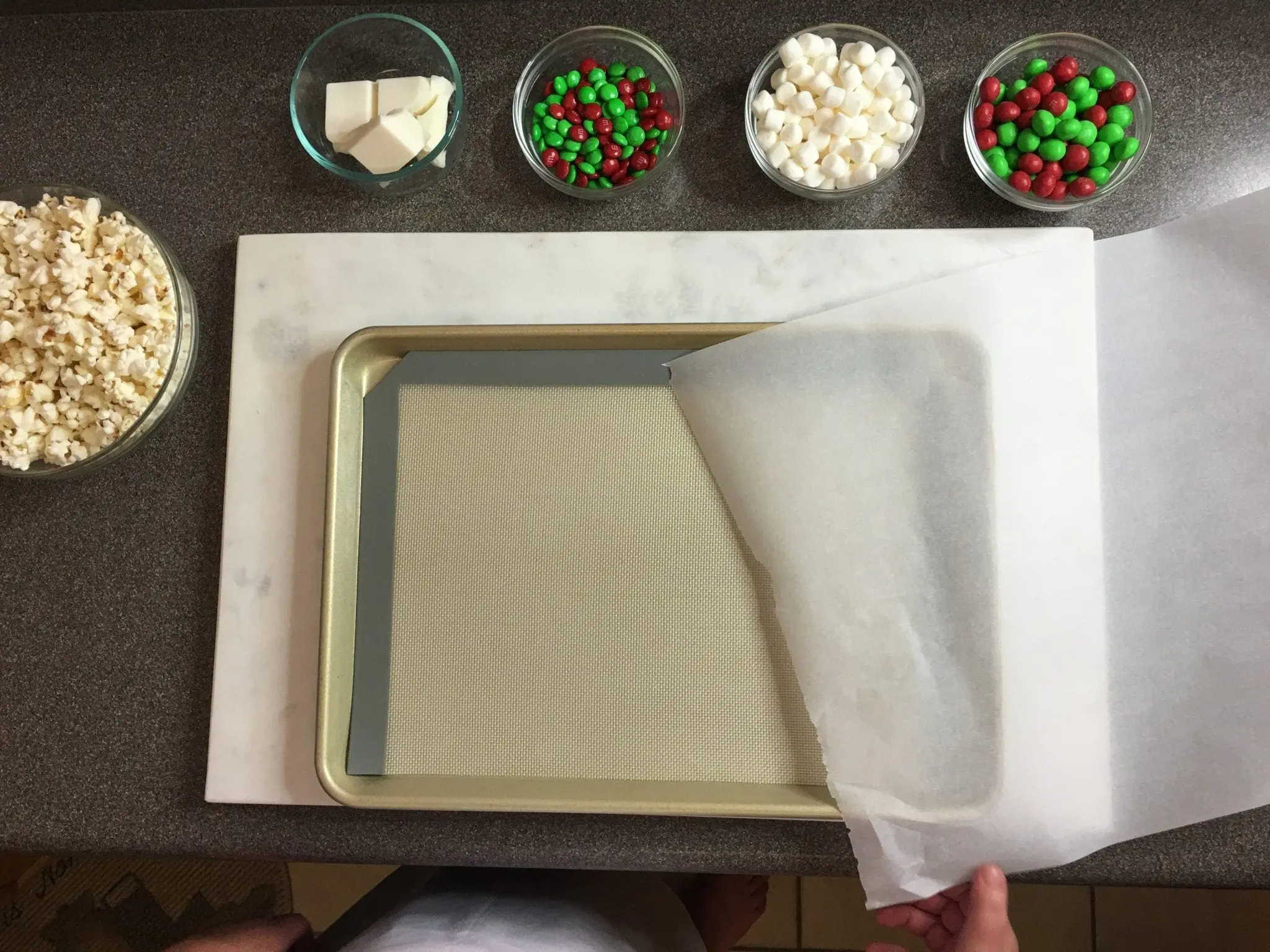 Popcorn, M&Ms, marshmallows, and almond bark are laid out on a counter next to a baking sheet.