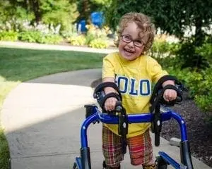 Benjamin smiling while using a gait trainer outdoors.