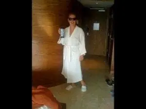 A person in a white robe and sunglasses holds a drink.