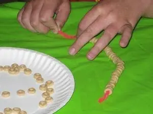 Child's hands threading cereal onto a pipe cleaner to create a necklace.