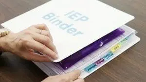 White IEP binder with colorful tabs being held by hands.