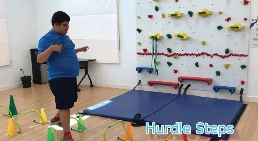Young person navigates a series of hurdles and steps in a gym.
