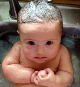 Baby with Down syndrome in a sink with soapy hair.