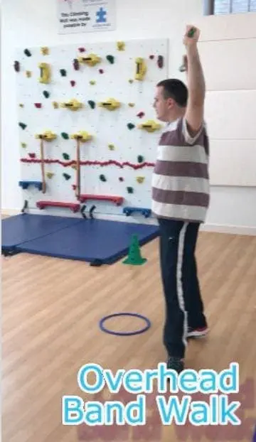 Man performing an overhead band walk in front of a climbing wall.
