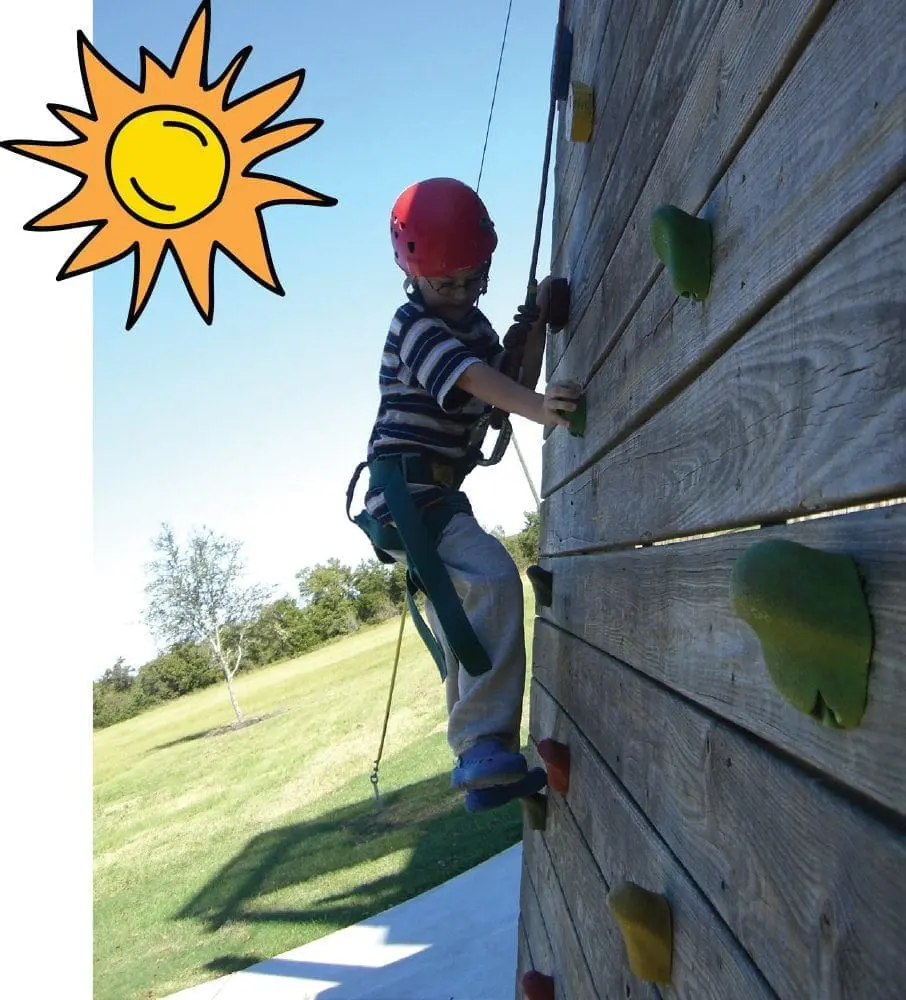 A child in a red helmet climbs a wooden wall with colorful holds.