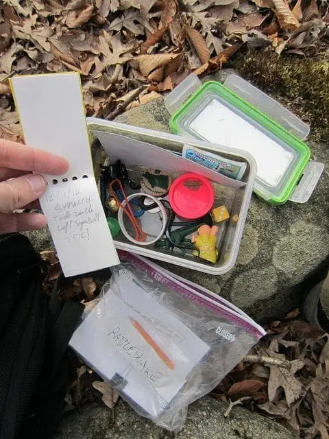 A hand holds a spiral notebook over a plastic container filled with small items and a ziplock bag with papers.